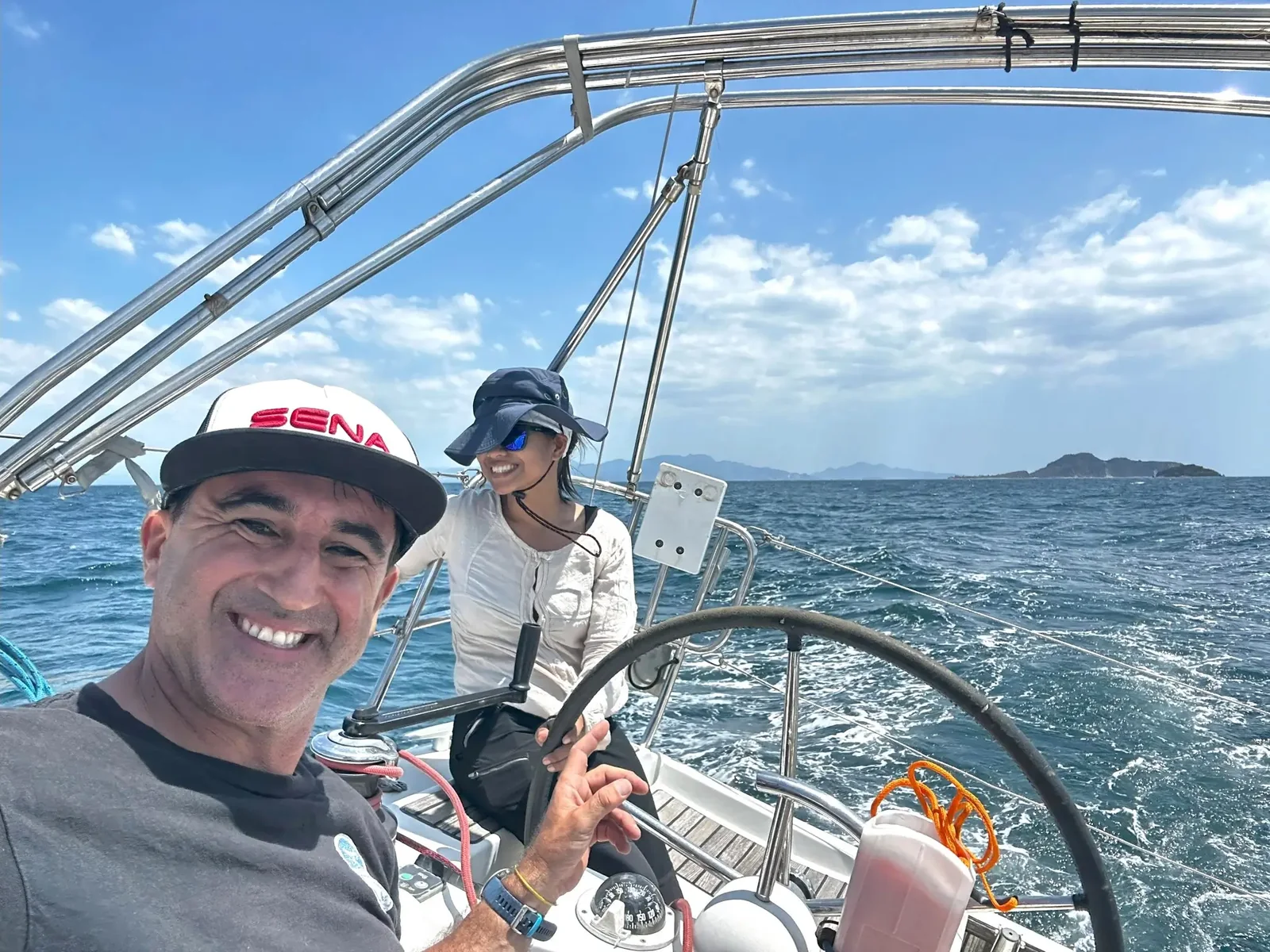 Smiling guests and skipper in the cockpit of a yacht under sail on a sunny day