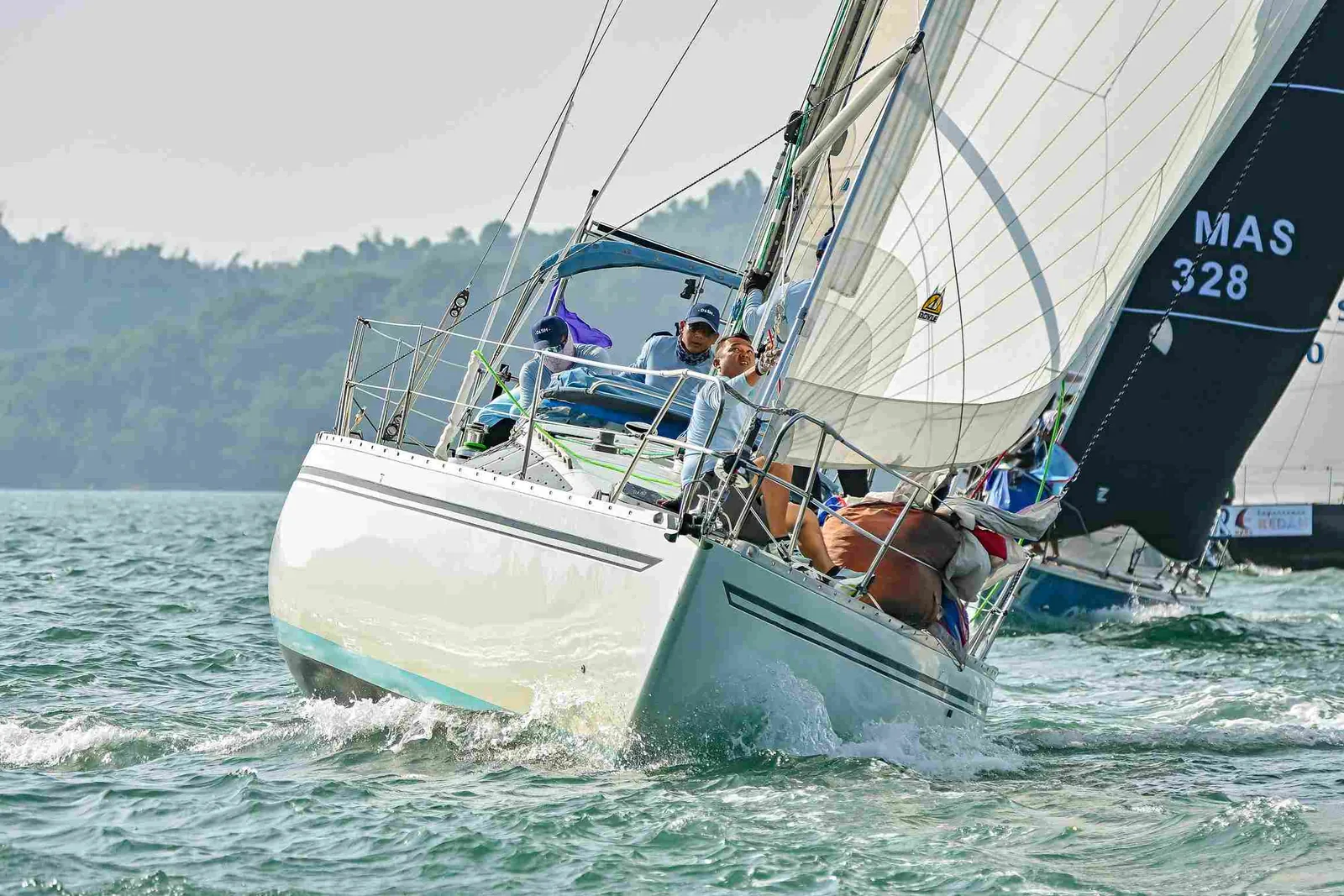 Two keelboats racing close together under full sail with a mountainous coastline behind