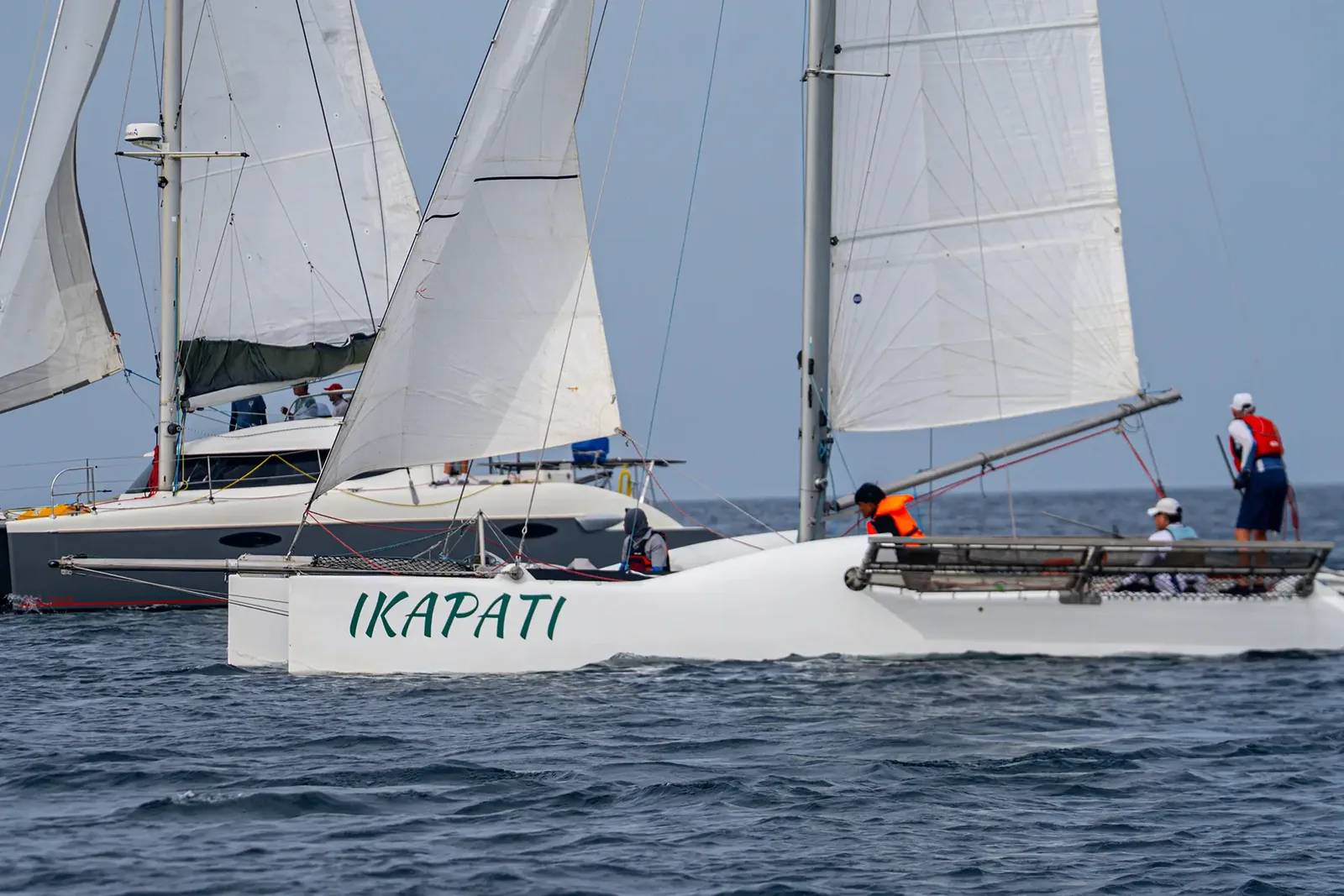 Crewed multihull sailing upwind alongside a keelboat during a race