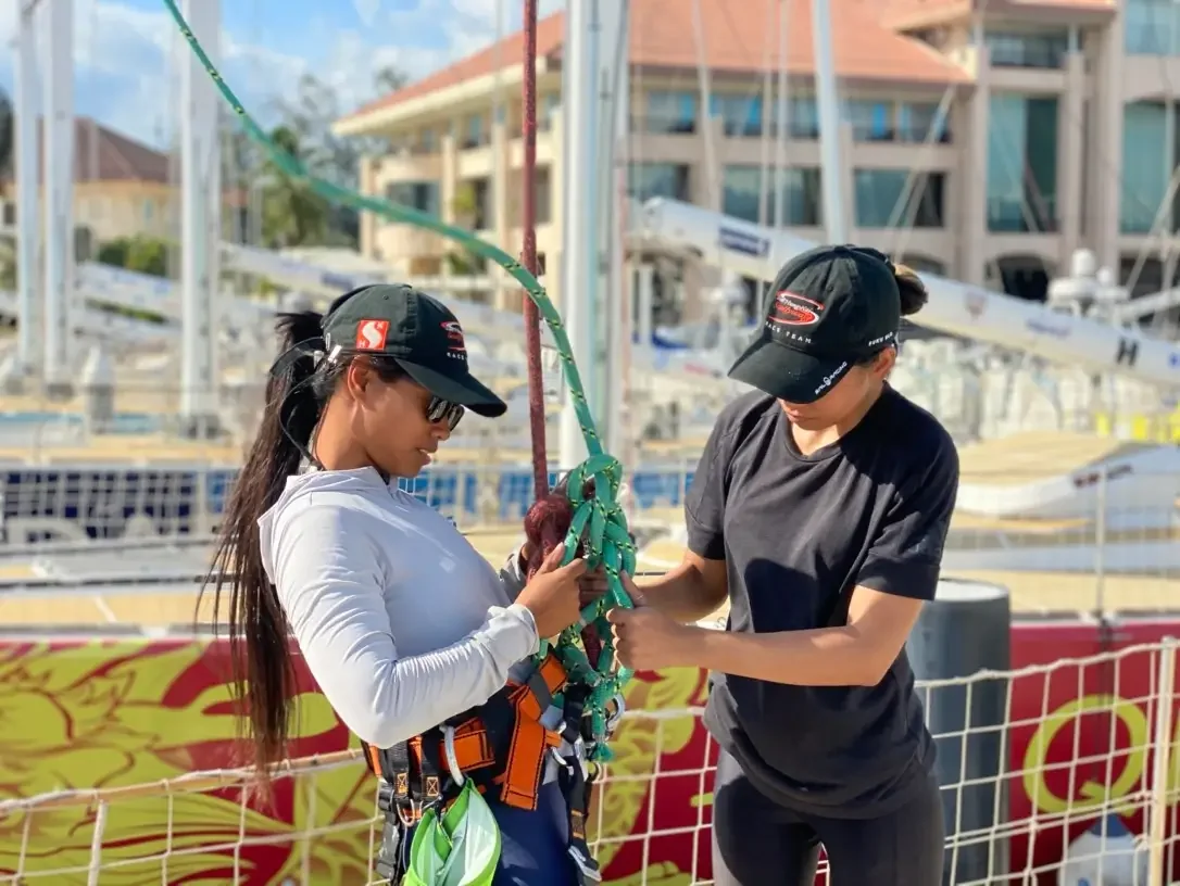 Two crew members checking lines and safety gear on a yacht alongside a marina berth