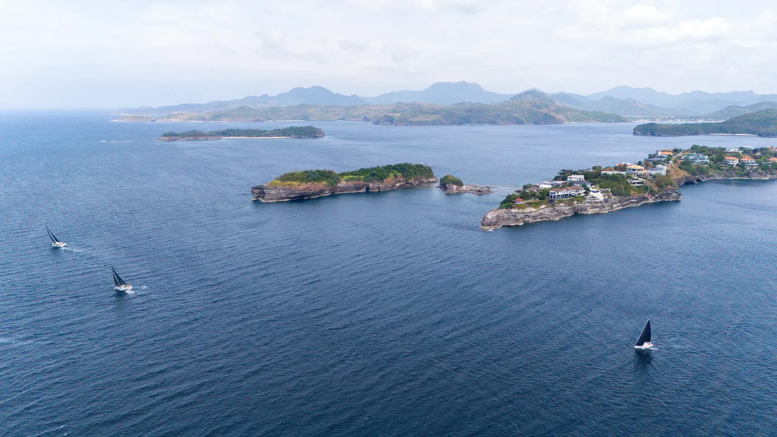 Aerial view of a sailing fleet passing a cluster of tropical islands